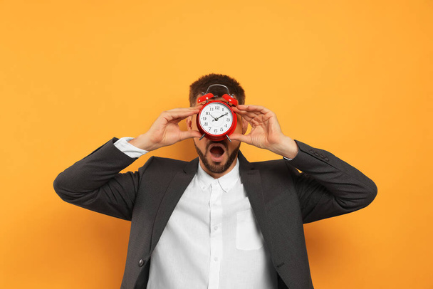 Emotional man with alarm clock on orange background. Being late concept - Photo, image