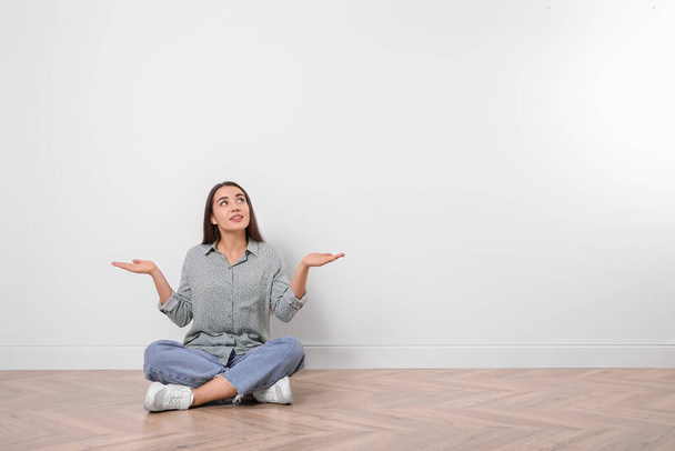 Young woman sitting on floor near white wall indoors. Space for text - Фото, зображення