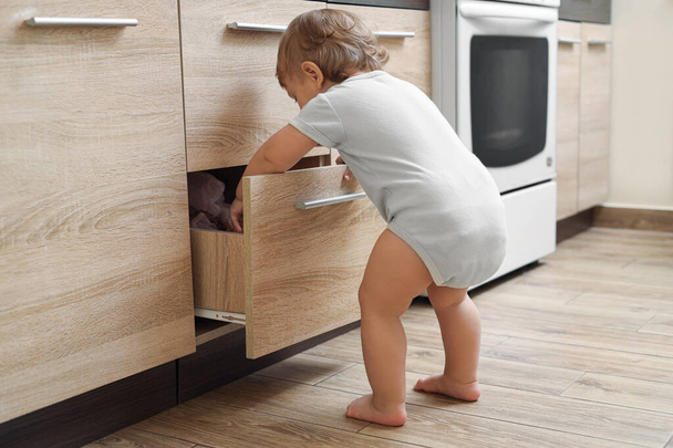 Little child exploring drawer in kitchen. Dangerous situation - Foto, afbeelding