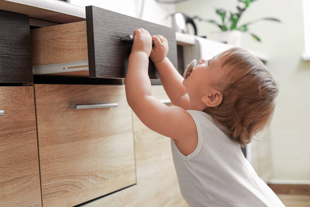Little child exploring drawer indoors. Dangerous situation - Foto, afbeelding
