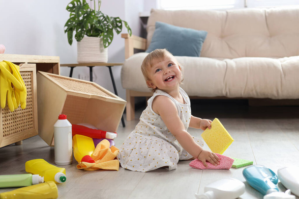 Cute baby playing with cleaning supplies on floor at home. Dangerous situation - Foto, Bild