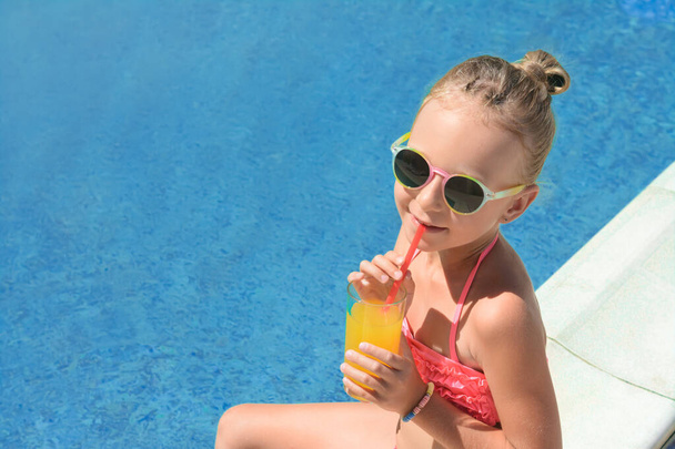 Cute little girl with glass of juice in swimming pool on sunny day. Space for text - Фото, зображення