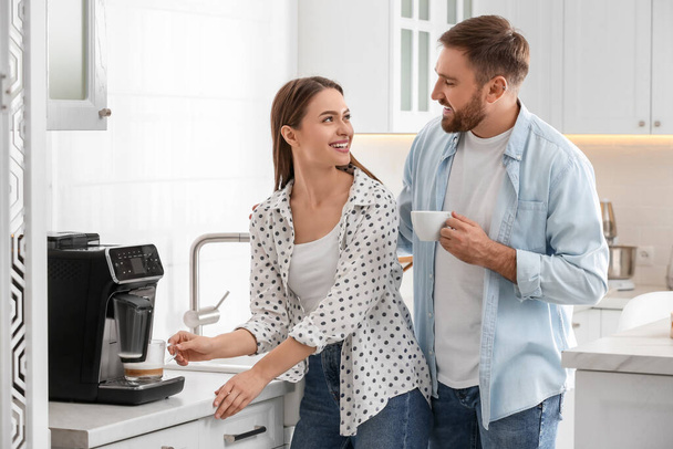 Happy couple preparing fresh aromatic coffee with modern machine in kitchen - Foto, Imagen