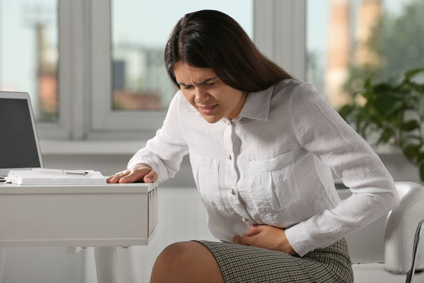 Young woman suffering from menstrual pain in office - Foto, imagen