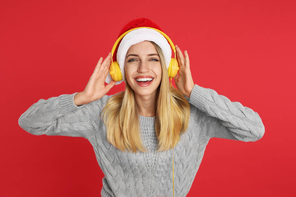 Happy woman with headphones on red background. Christmas music - Фото, изображение