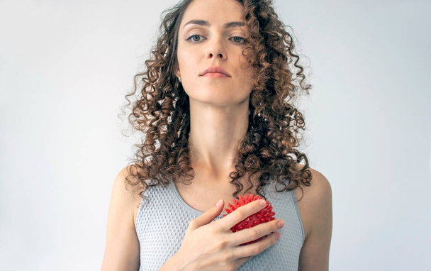Kudrnatá mladá žena provádí myofáziální uvolnění na prsní svaly pomocí ostnaté kuličky doma. Koncept: cvičení self-care s rekvizitami doma, self-massage - Fotografie, Obrázek