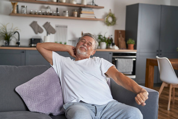 Älterer Mann dehnt sich morgens und sitzt auf Couch   - Foto, Bild