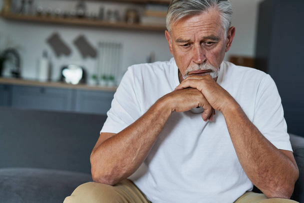 Idősebb fehér férfi mentális problémákkal otthon ül a kanapén - Fotó, kép