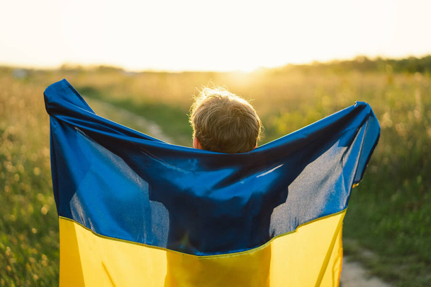 Den nezávislosti Ukrajiny. Chlapec v bílém tričku se žlutou a modrou vlajkou Ukrajiny v poli. Ukrajinská vlajka. Den ústavy. Stojan s Ukrajinou a Uložit - Fotografie, Obrázek