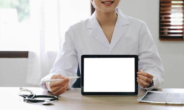 Portré tapasztalt orvos nő kardiológus jelen modern technológia fehér képernyős tabletta ő használ konzultáljon betegek viselnek fehér köpeny egységes sztetoszkóp a vizsgálóban - Fotó, kép