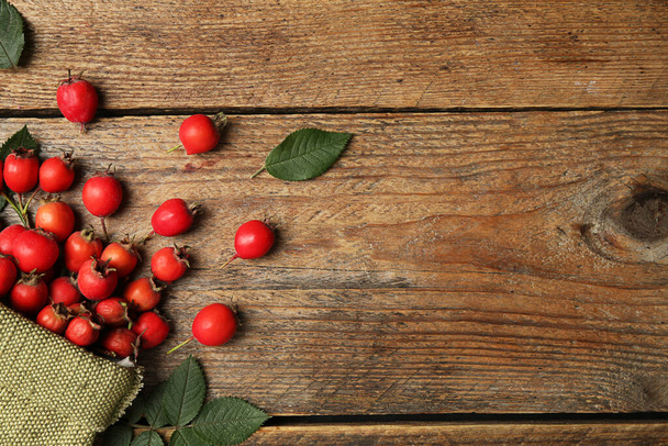 Ripe rose hip berries with green leaves on wooden table, flat lay. Space for text - Фото, зображення