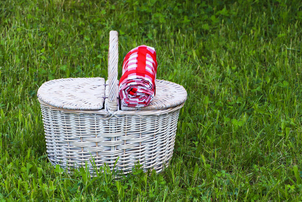 Rolled checkered tablecloth with picnic basket on green grass outdoors, space for text - Фото, изображение