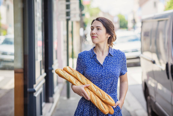 Young pretty woman buying a french baguette and standing on the street in city - Foto, Bild