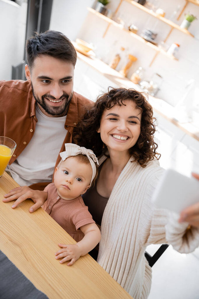 mujer rizada tomando selfie con alegre marido y bebé hija en casa - Foto, Imagen