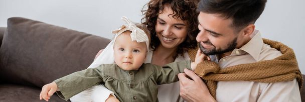 genitori positivi guardando la neonata in fascia in soggiorno, striscione - Foto, immagini