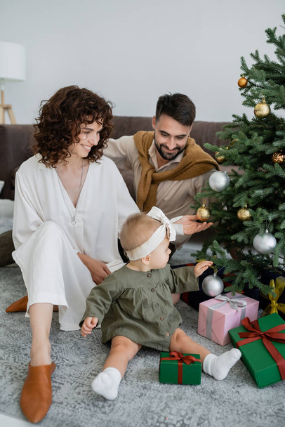 happy family with infant baby girl sitting near christmas tree with presents  - Φωτογραφία, εικόνα