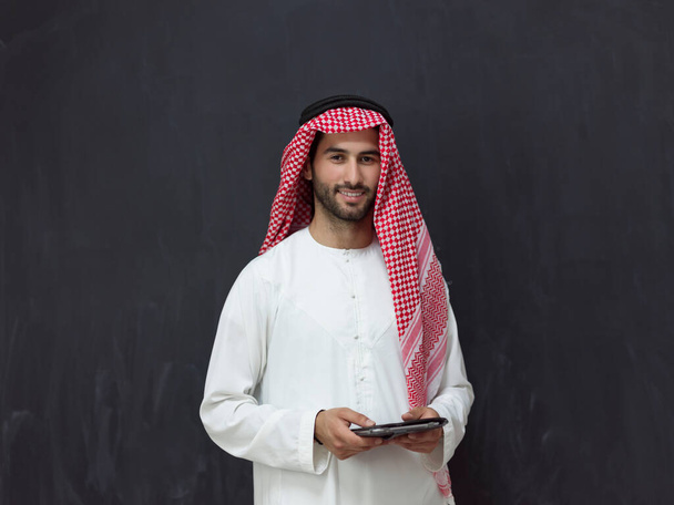Young Arabian Muslim businessman using a tablet computer wearing hijab clothes in front of a black chalkboard. High quality photo - Foto, Imagen