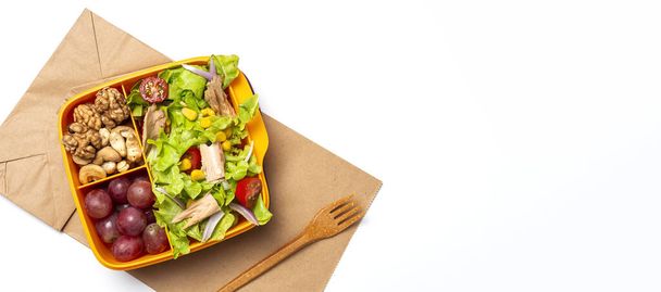 Healthy Food in Plastic container ready to eat with homemade lettuce salad with tomato, onion, corn, tuna, roga grapes, walnuts and cashews in paper bag fro, above. Take away concept - Foto, Imagen