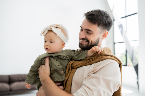 cheerful bearded man holding in arms and looking at infant baby in headband  - Foto, Imagem