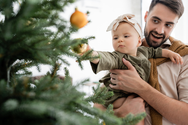 excited father holding infant daughter near decorated christmas tree - 写真・画像