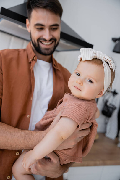 happy man with beard holding in arms baby daughter in headband  - 写真・画像