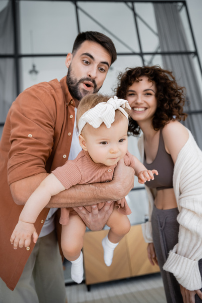 excited bearded father holding in arms baby daughter near cheerful wife at home - Foto, imagen
