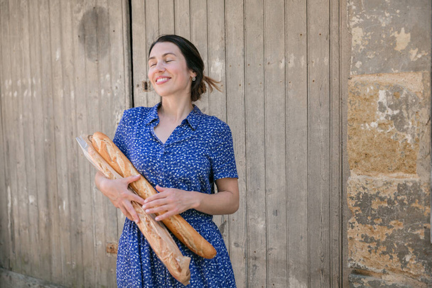 Young pretty woman standing with french baguettes in her hands in the countryside - Foto, imagen