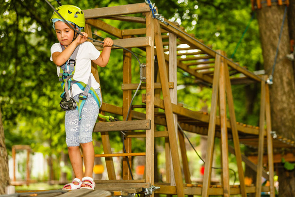 Retrato de niña sonriente en casco y arnés en pista en cielo cuerda parque en verano - Foto, Imagen