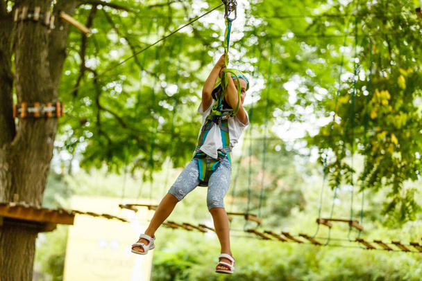 Ragazza felice scuola godendo di attività in un parco avventura arrampicata in una giornata estiva - Foto, immagini