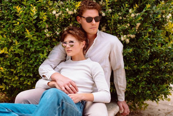 Young beautiful hipster couple in love sitting on old city park, summer Europe vacation, travel, fun, sunglasses, trendy outfit, romance, date, embracing - Photo, image