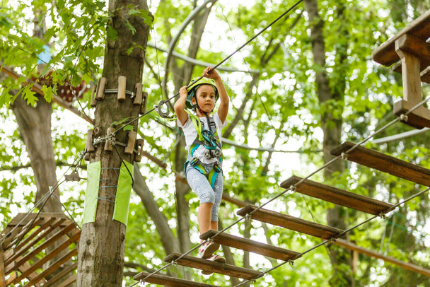 Liebenswertes kleines Mädchen genießt ihre Zeit im Klettererlebnispark an einem warmen und sonnigen Sommertag. Sommeraktivitäten für kleine Kinder. Kind hat Spaß in den Schulferien. - Foto, Bild