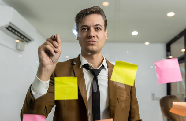 Business people holding pen and put sticky notes on glass wall in office. business people meeting at office and use post it notes to share idea. brainstorming concept. - Фото, зображення