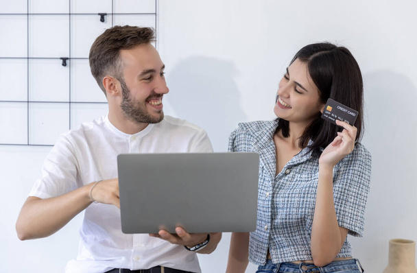 Couple consumer holding credit card and laptop buying online at home. Woman and Man shipping online with credit card in hand. Couple using laptop technology paying credit card shopping online - Photo, Image