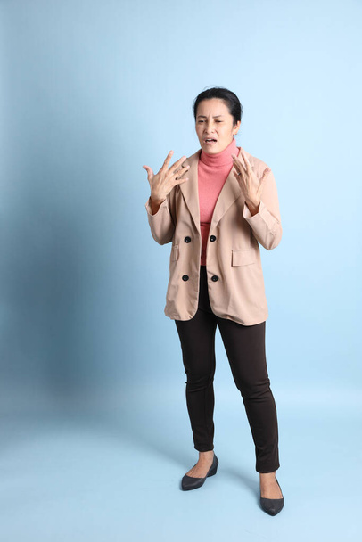 The senior Asian woman with pink shirt brown blazer on the blue background. - Foto, Imagen