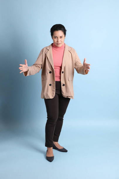The senior Asian woman with pink shirt brown blazer on the blue background. - Foto, imagen