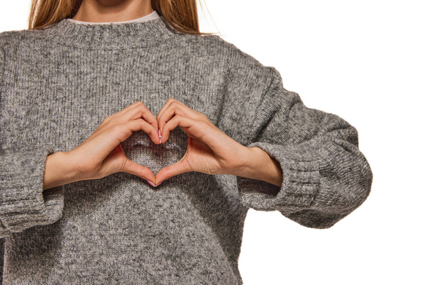 Unrecognizable woman in warm grey sweater showing heart shape isolated over white background. Love, hope, people affection and care concept. Support, and peace in the world - Фото, зображення