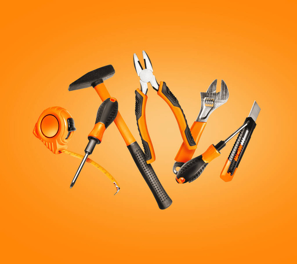 Новые строительные инструменты в воздухе на оранжевом фоне - Фото, изображение