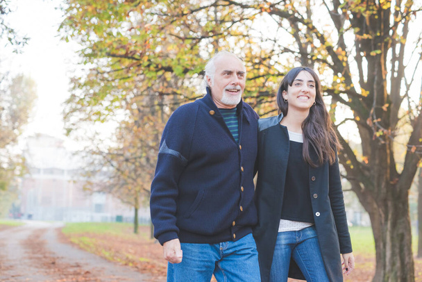Adult father and daughter relaxing together walking arm in arm outdoors in autumn - Photo, image