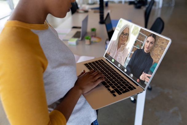 Midsection of african american businesswoman discussing on videocall with coworkers over laptop. Unaltered, office, meeting, teamwork, business, communication and technology concept. - Zdjęcie, obraz