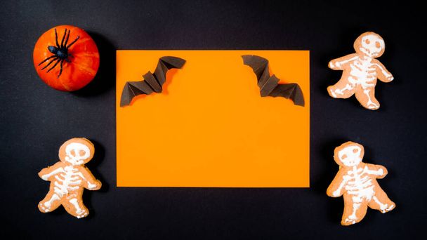 Netopýr na oranžovém pozadí v černém obdélníkovém rámu zdobeném malou oranžovou dýní s černým pavoukem a perníčkem ve tvaru kostry. Halloween dovolená koncept. - Fotografie, Obrázek