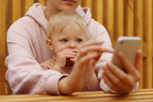 Portrait of fasceless woman sitting and using cell phone, holding baby daughter in hands, unknown female typing on mobile phone, checking social networks. - Foto, Imagem