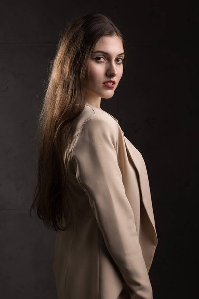 Portré egy fiatal barnáról, hosszú hajjal a stúdióban. Drámai fotó sötét színekben. - Fotó, kép
