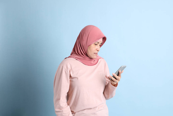 Vanhempi Kaakkois-Aasian nainen hijabilla seisoo sinisellä taustalla - Valokuva, kuva