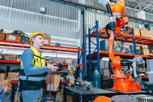 Καυκάσιος μηχανικός αρσενικός εργαζόμενος που εργάζεται στο εργοστάσιο μετάλλων με τον ελεγκτή προγραμματιστών μηχανών συγκόλλησης ρομπότ και παρακολουθεί. - Φωτογραφία, εικόνα