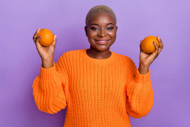 Photo of cute young woman hold oranges eat healthy fruits dressed trendy autumn orange knitwear sweater isolated on violet color background. - Photo, Image