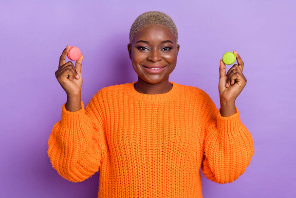 Photo of charming young lady hold two macaroons cookies dressed stylish autumn orange knitted sweater isolated on violet color background. - Foto, Imagem