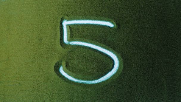 Ötös számú kézi rajz 5. szimbólum a zöld homokban. A férfi kéz ráír egy számot a zöld homokra, háttérvilágítással. Ez egy sorozat 0-tól 10-ig. Felülnézet 4k felbontás - Fotó, kép