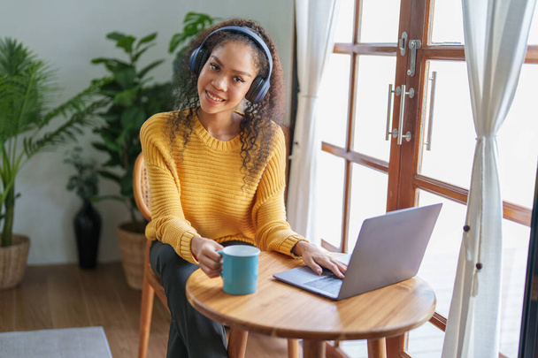 Retrato de un afroamericano con auriculares sosteniendo una taza de café y usando una computadora. - Foto, imagen