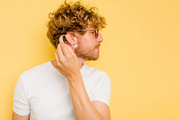Young caucasian man wearing hearing aid isolated on yellow background - Foto, immagini