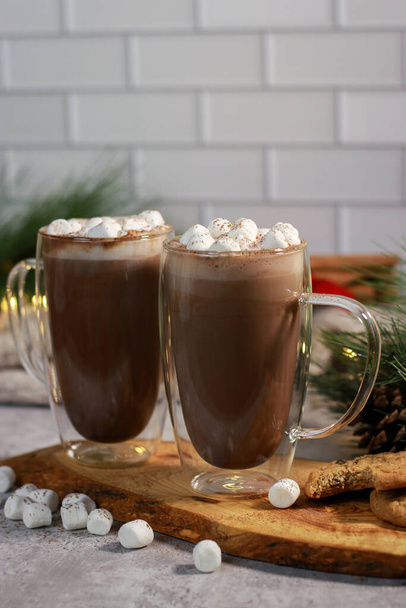 hot chocolate in a glass mug with mini marshmallows on grey table with cookies, mandarins and cinnamon sticks, blurred xmas decoration background . High quality photo - Valokuva, kuva